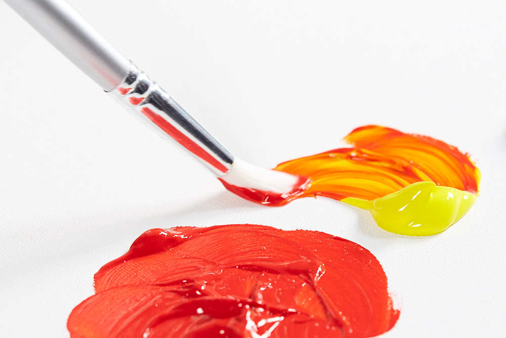 A synthetic artists paint brush being used to apply fluid acrylic colour