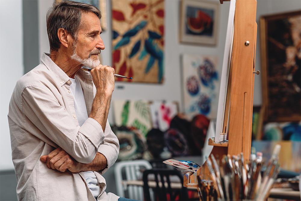 Side view of a thoughtful artist holding paintbrush while sitting in his studio