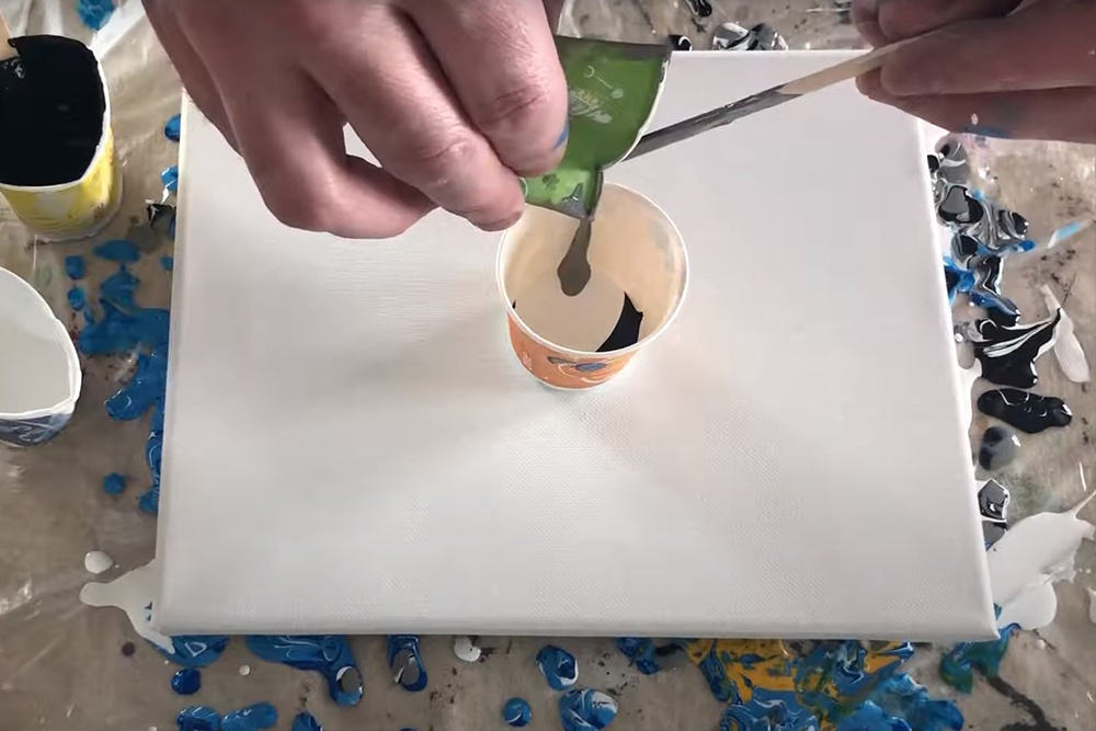 Artist layering fluid acrylic paint in a cup ready for a dirty pour