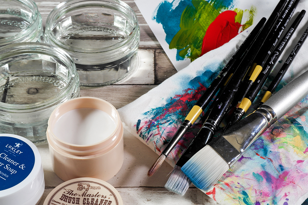 Assorted Acrylic Brushes on a paint rag with brush soaps and jars of water.