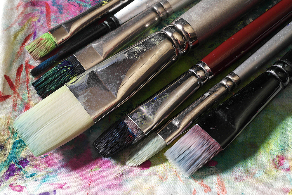 Assorted clean and dirty acrylic painting brushes on a painters rag.