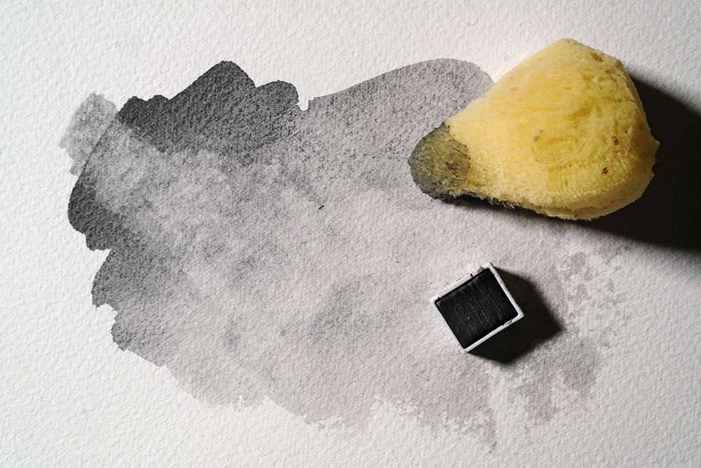 A sponge is used to lift colour from a wet wash of Graphitint Graphite Grey to create wispy greys.