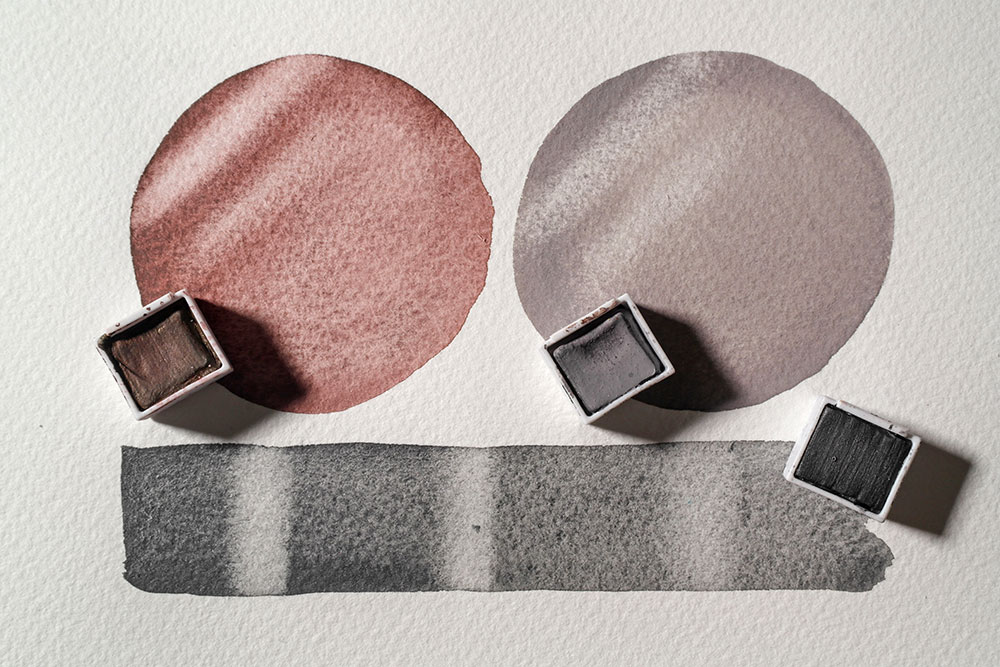 Two circular swatches of Graphitint Autumn Brown and Pastel Shades Storm Grey, witha rectangular swatch of Graphitint Graphite Grey below. The swatches are dry and an eraser has been used to lift colour.
