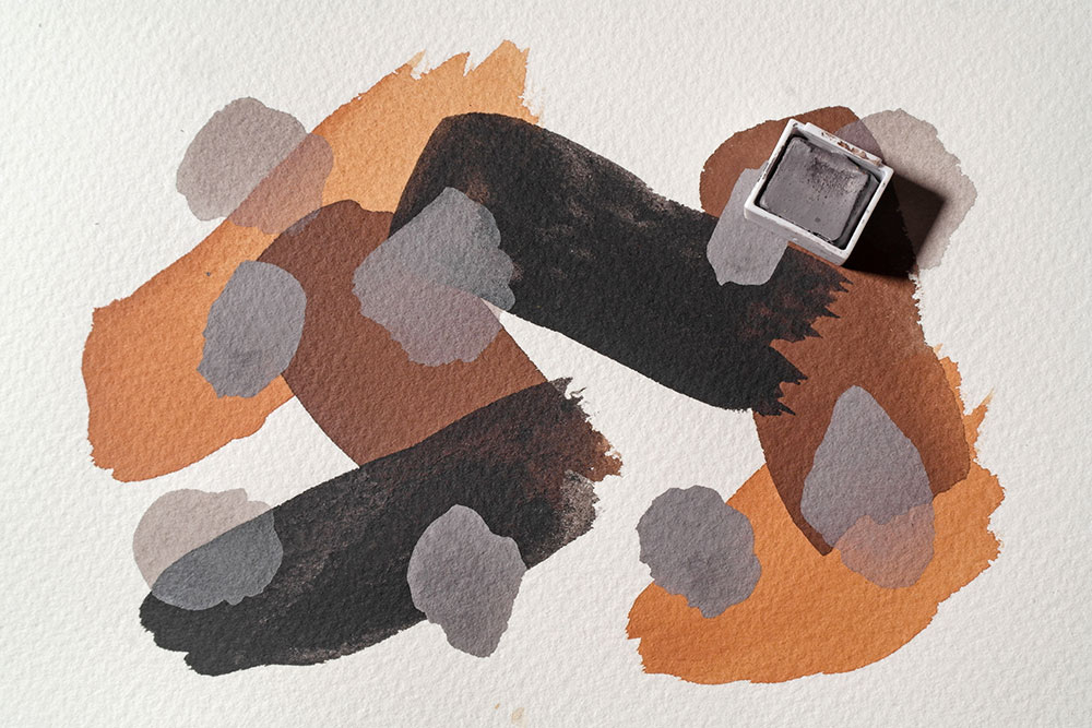 Bold strokes of Derwent Inktense paint cover a sheet of watercolour paper. Blobs of Storm Grey Pastel Shade has been layered over the top in various opacities.