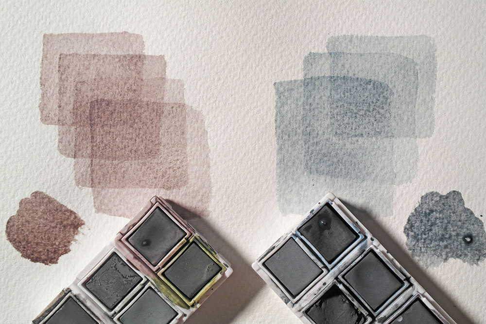 Painted swatches of layered colour (Glowing Embers and Mountain Blue) from the Derwent Tinted Charcoal Paint Pan Set.