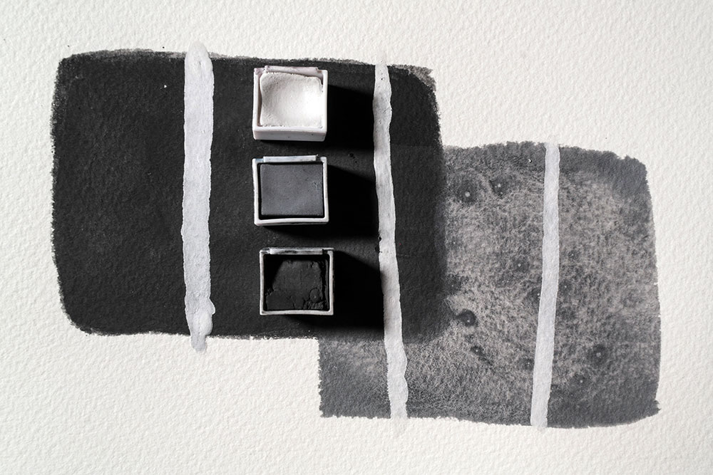 A thick mixture of opaque White Tinted Charcoal paint is layered over the top of a dried swatch of Dark and Natural paint.