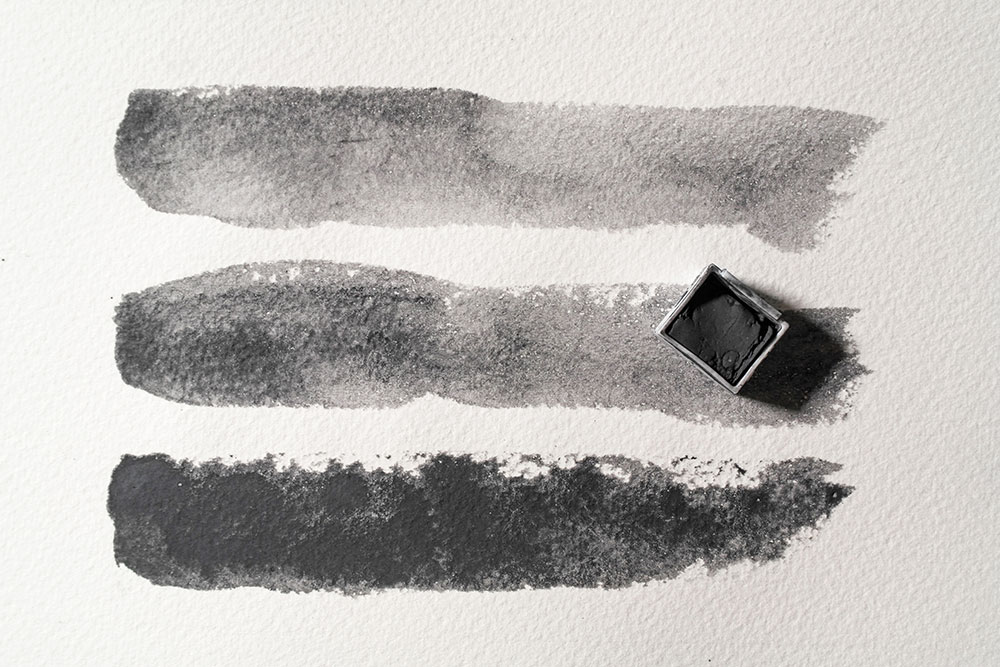 Painted strokes of Derwent Tinted Charcoal in Dark (Black). The top stroke is diluted with water, the middle swatch with less water and the bottom with even less.