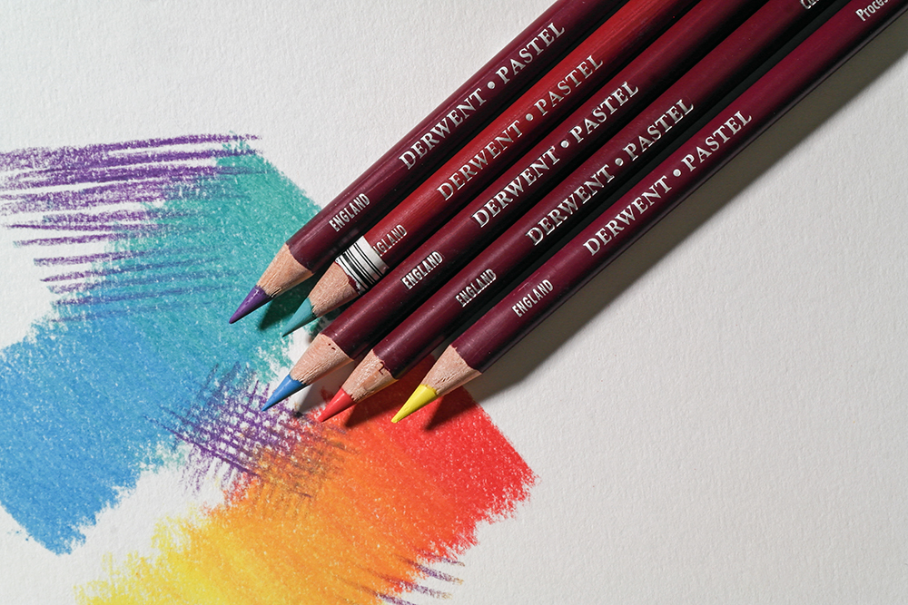 Vary your mark making techniques to add interest - Derwent Pastel Pencils in purple, turquoise, blue, red and yellow are photographed next to smooth blended pastel marks and cross hatching.