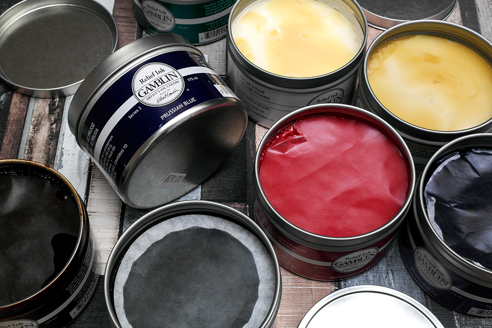 Metal tubs of Gamblin Relief Printmaking Inks on a dark wooden background