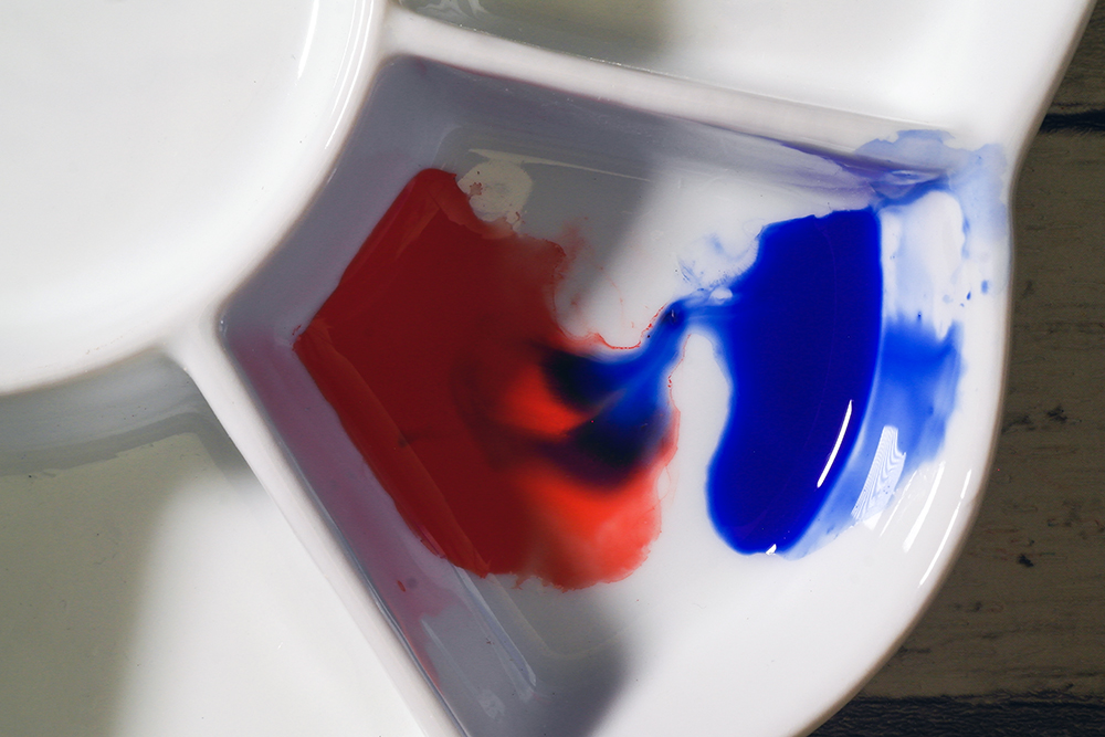 A ceramic palette with a mixture of red and blue watercolour paint.