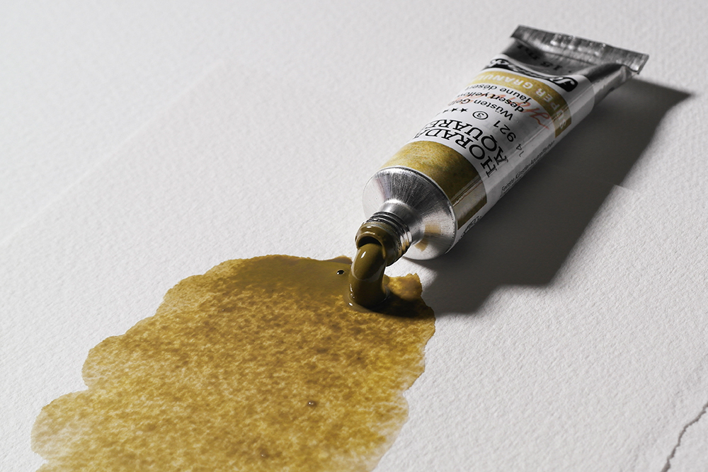 A tube of Schmincke Horadam Super Granulating Watercolour Paint in Desert Yellow is squeezed onto a sheet of paper.