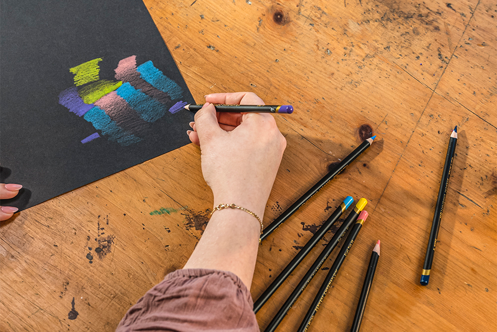 Artist using assorted Chromaflow colouring pencils on a sheet of black paper