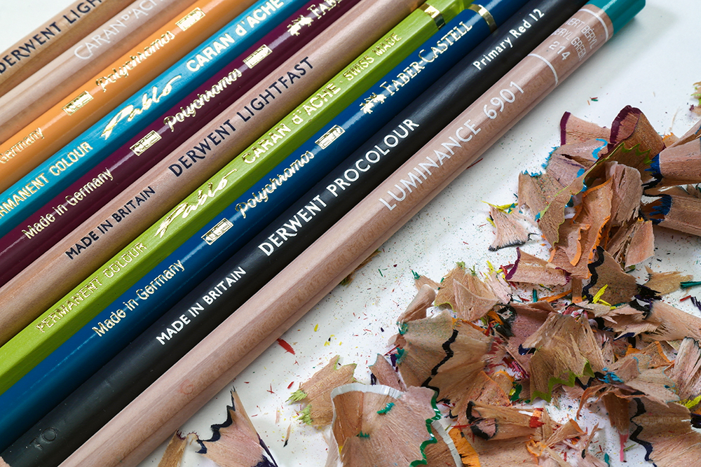 Photograph of pencil barrels showing brand names like Derwent, Faber-Castell and Caran d'Ache alongside pencil shavings.