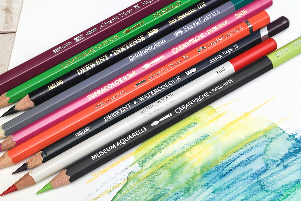 The wooden barrels of assorted artists' watecolour pencils showing brand names like Caran d'Ache, Derwent and Faber-Castell.