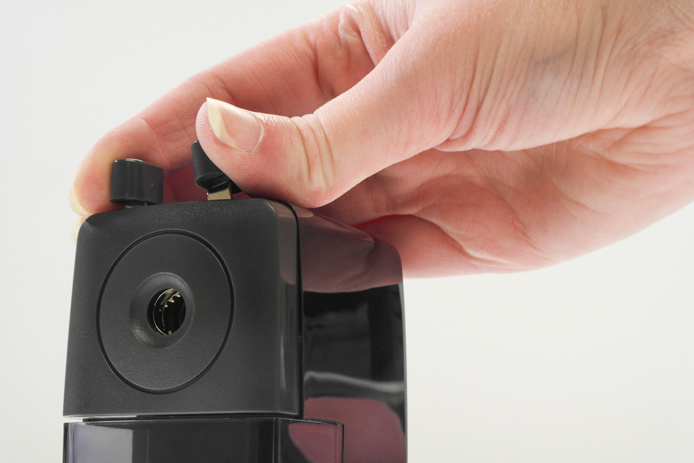 Artists hand moving pincers on the top of a crank pencil sharpener.