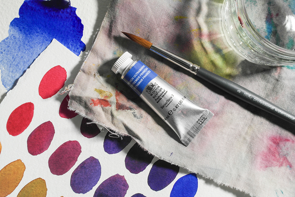 A tube of French Ultramarine with a brush and hand painted colour mixing charts