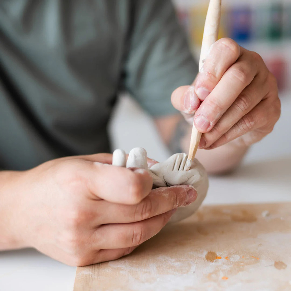 A sculptor using a wooden sculpting tool to shape clay.