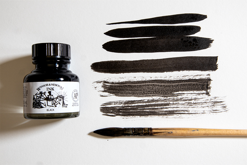A bottle of Winsor & Newton Black Indian Drawing Ink and a quill brush alongside some hand painted brush strokes.