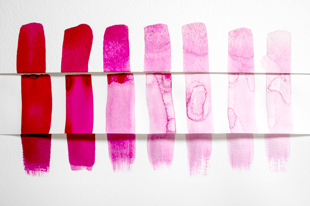 Swatches of magenta drawing ink painted in different strengths along three different types of paper.
